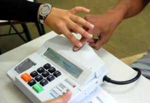 homem pegando na mão de outra pessoa no leitor de biometria da urna eletrônica para mostras que as Mais de 53% dos eleitores de Passo Fundo são mulheres