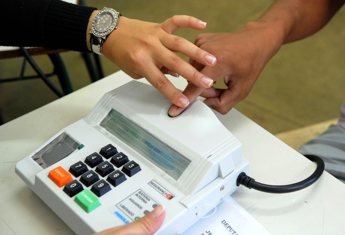 homem pegando na mão de outra pessoa no leitor de biometria da urna eletrônica para mostras que as Mais de 53% dos eleitores de Passo Fundo são mulheres