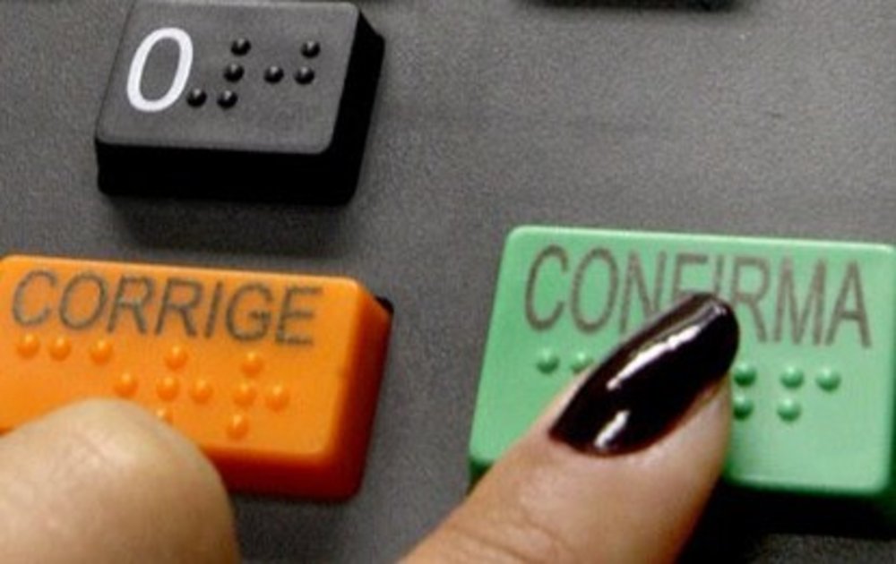 Dedo feminino pressionando a tecla confirma da Urna Eletrônica